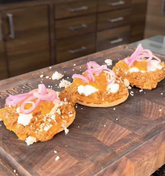 Tres tostadas montadas con chicharrón en salsa tatemada, crema y cebolla morada sobre una tabla