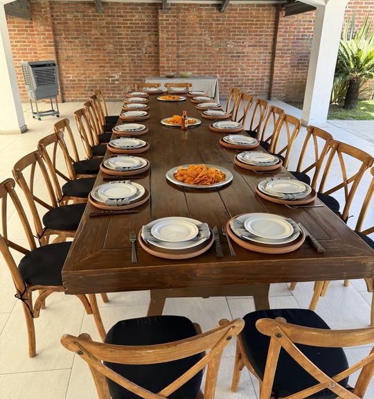 Mesa larga bajo una pérgola de madera con sillas cross-back y vajilla puesta